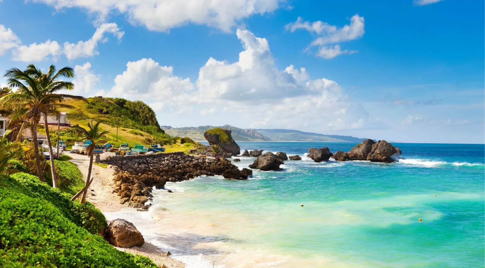 Rocks and fishing boats on the rugged Atlantic coast of Barbados under a blue sky