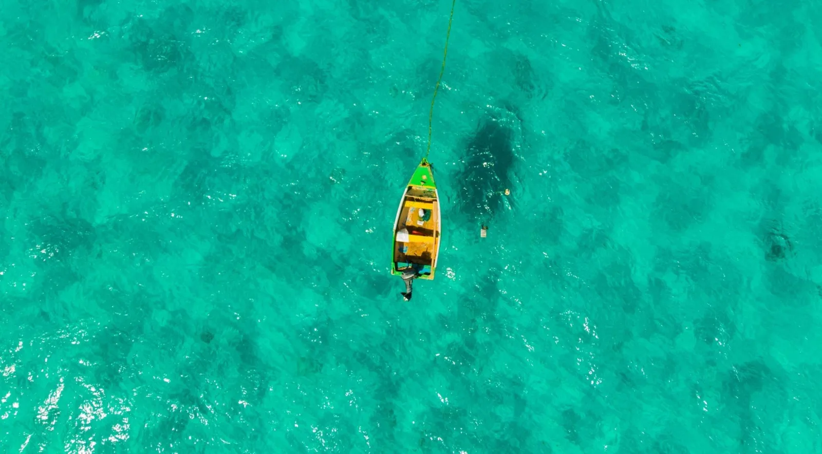 Aerial view of a small green fishing boat moored alone on flat turquoise water