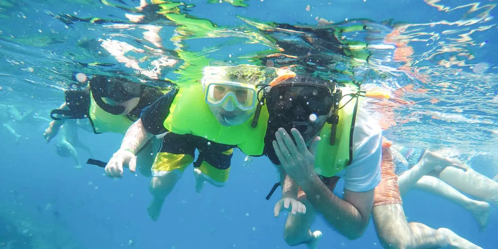 Three snorkellers in bright flotation vests floating face-down at the surface