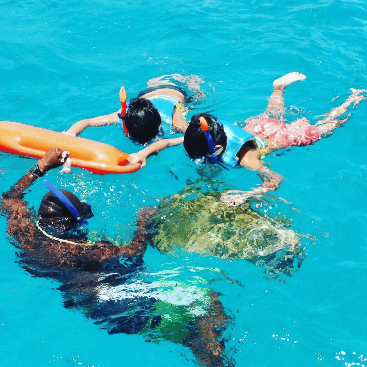 A guide holding a float while two children snorkel above a sea turtle just under the surface