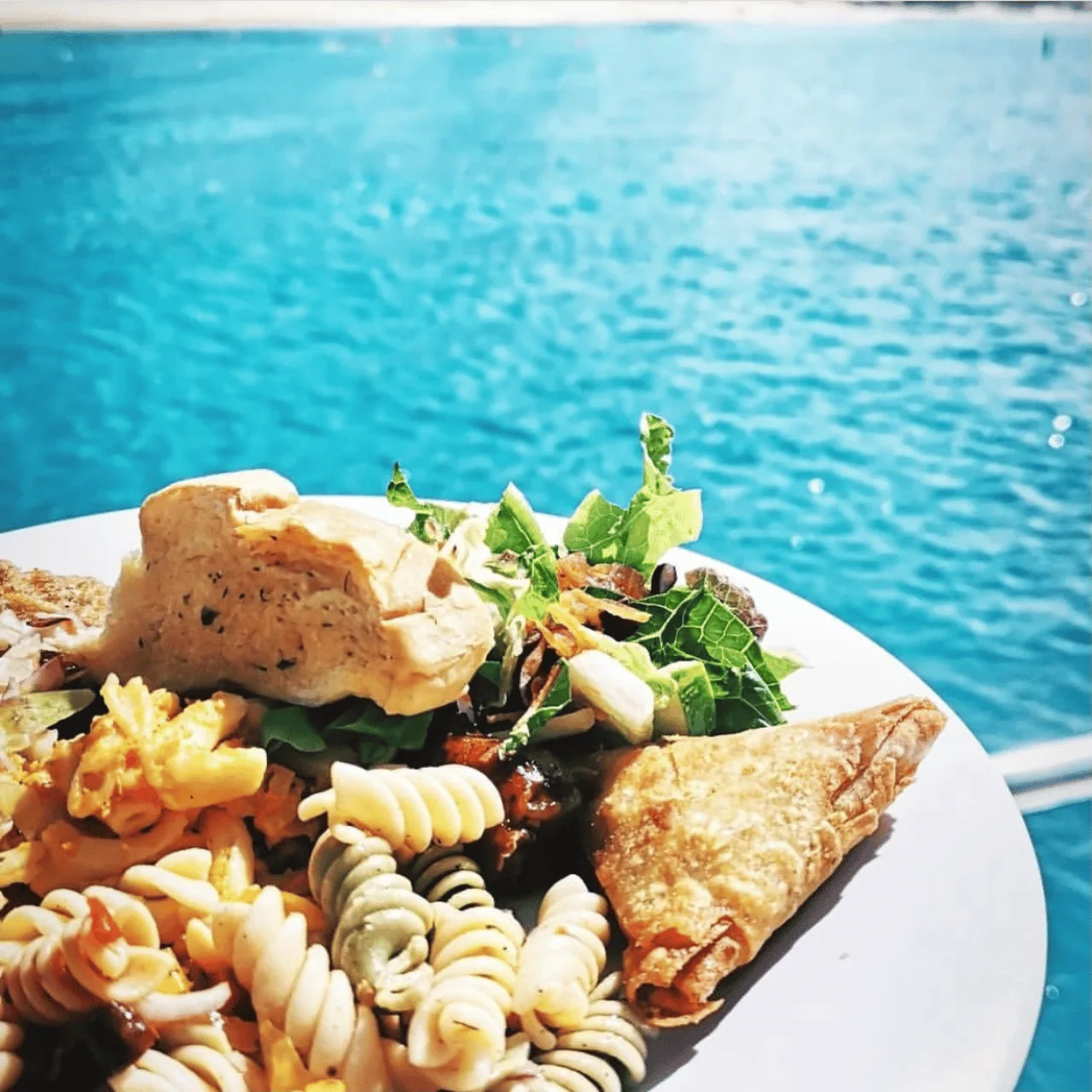 A buffet plate of pasta salad, macaroni pie and a pastry held above the water