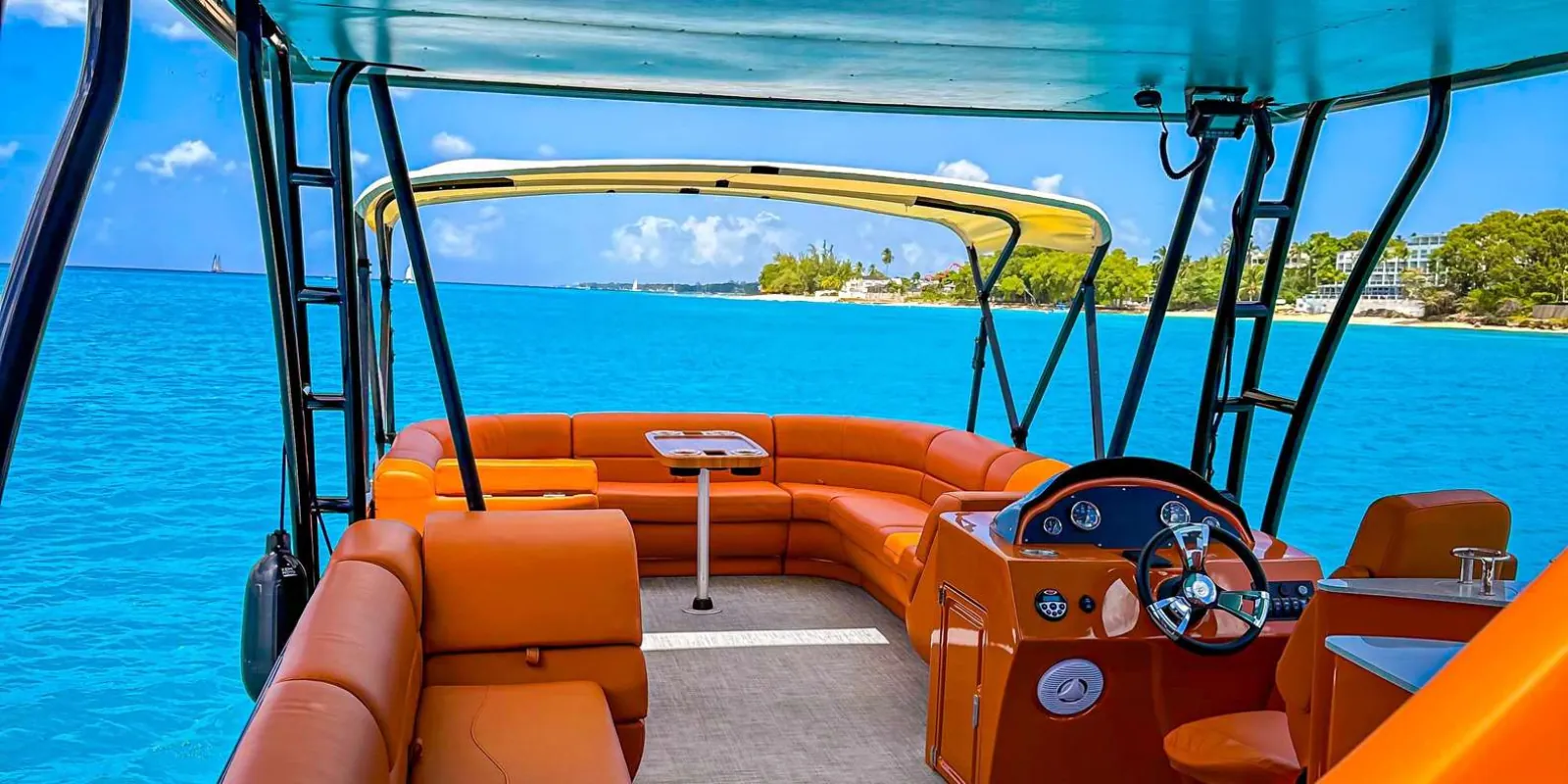 The pontoon's empty lower deck, orange seating and helm, looking out over turquoise water