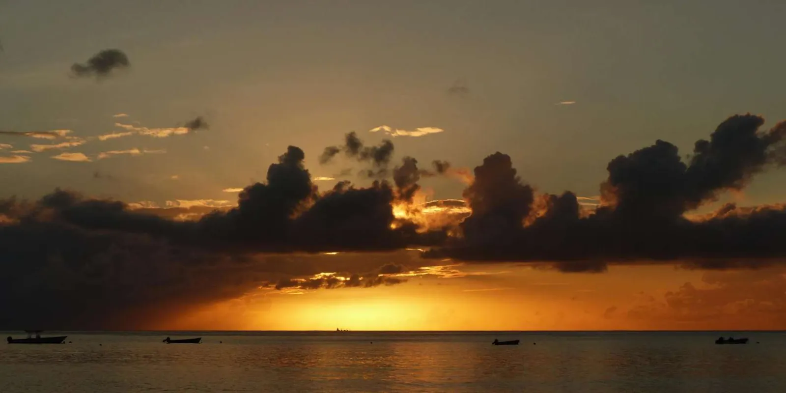 The sun setting behind cloud on the horizon with small boats moored in silhouette
