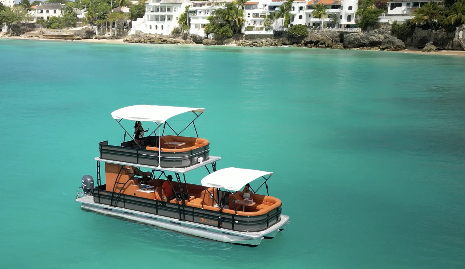 The double-decker pontoon anchored off a west coast beach with guests on the upper deck