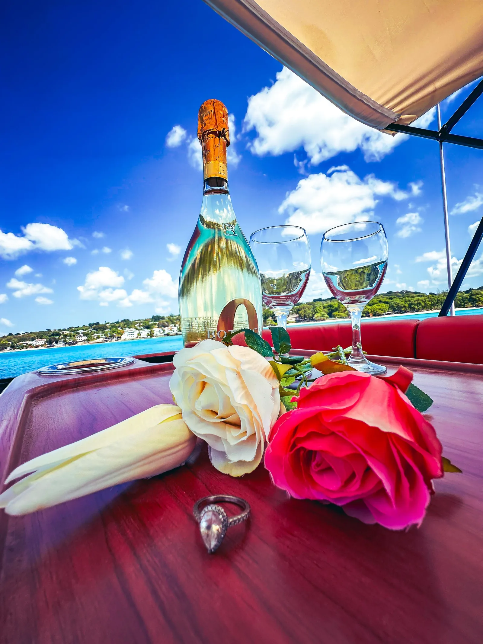 Sparkling wine, roses and an engagement ring set out on the boat's table