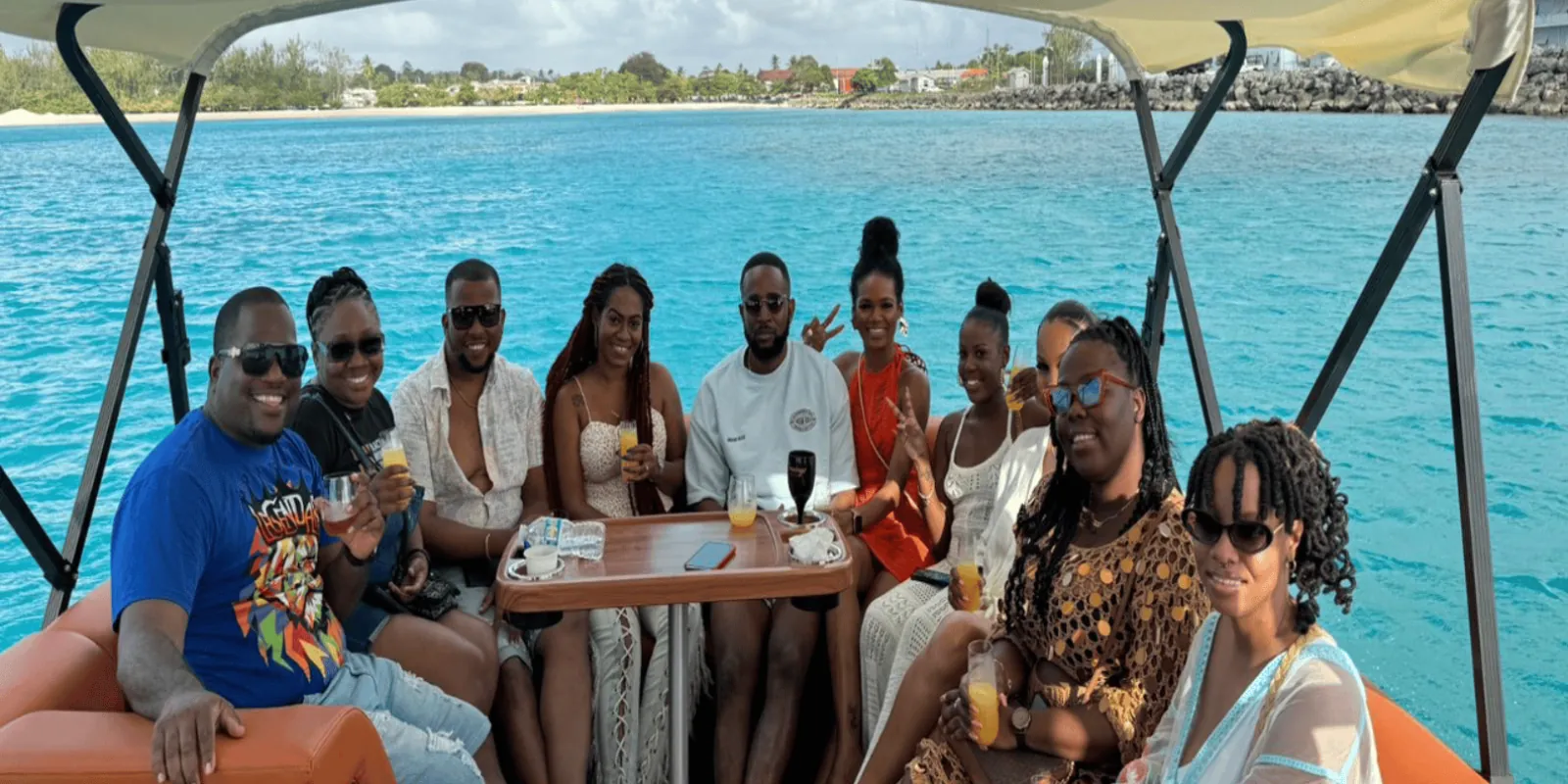 Guests with drinks around the table on the pontoon's lower deck, the coast behind them